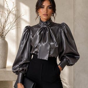 Blusa prateada metálica de cetim com mangas bufantes, gola alta vitoriana e laço grande.