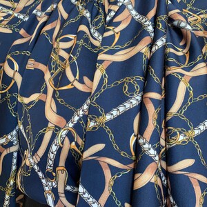 May include: A navy blue blouse with a pattern of gold chains and brown straps. The fabric is silky and has a slight sheen.