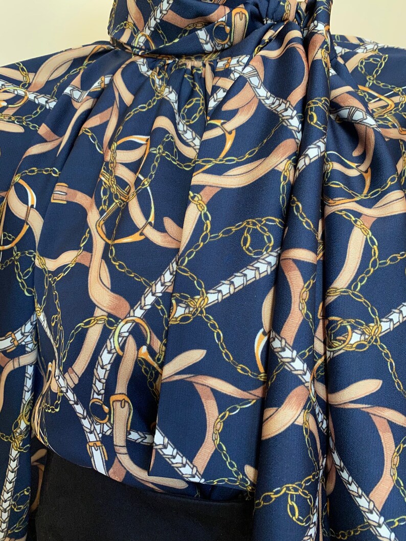 May include: A navy blue blouse with a pattern of gold chains and brown straps. The fabric is silky and has a slight sheen.