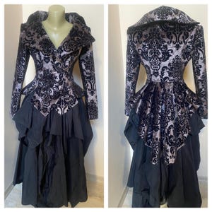 May include: A black and silver brocade jacket with a large collar and a fitted waist. The jacket is paired with a black skirt with multiple layers of ruffles.