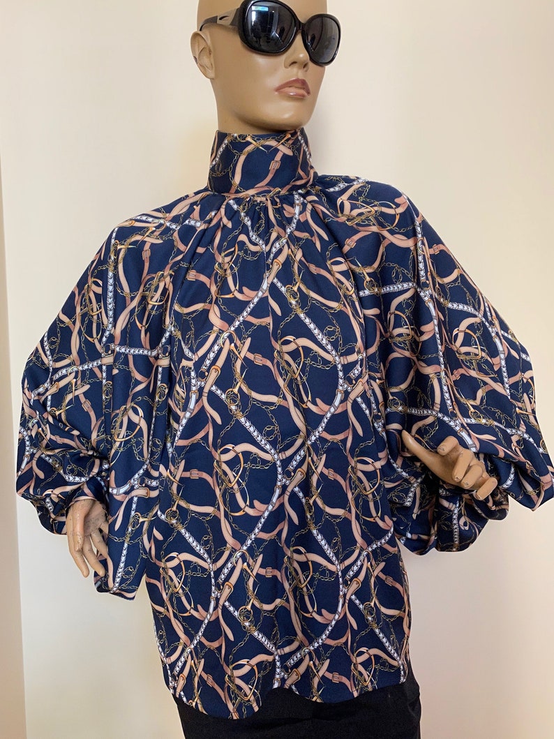 May include: A navy blue blouse with a high neck and long sleeves. The blouse has a pattern of gold chains and pink ribbons.