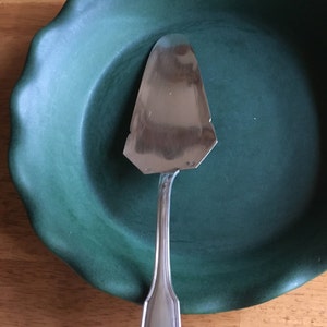 May include: A silver pie server with a decorative shell design on the handle sits on a green pie plate.