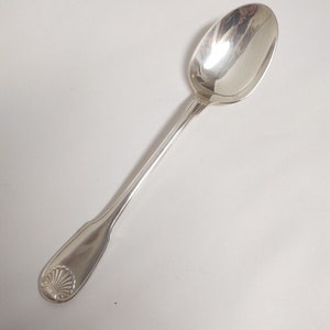 Op de afbeelding: Een zilveren lepel met een sierlijk schelpontwerp op de steel.
