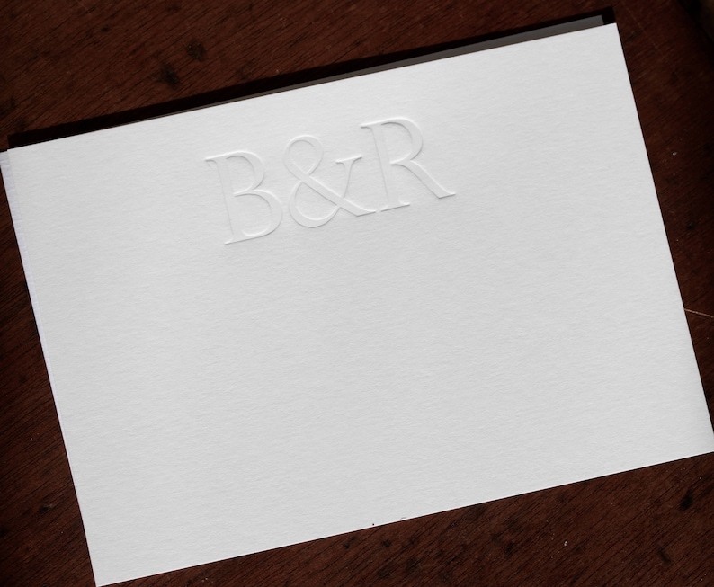 Pode incluir: Um cart&atilde;o branco com as letras B&R em relevo na parte superior central do cart&atilde;o.