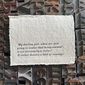 Puede incluir: Un trozo rectangular de papel hecho a mano con bordes irregulares, con la cita: 'My darling girl, when are you going to realise that being normal is not necessarily a virtue? It rather denotes a lack of courage.' Sobre un fondo de bloques de tipografía antiguos.