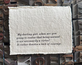 May include: A rectangular piece of handmade paper with deckled edges, featuring the quote: 'My darling girl, when are you going to realise that being normal is not necessarily a virtue? It rather denotes a lack of courage.' The paper rests on a background of vintage letterpress blocks.