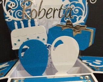May include: A blue and white pop-up card with the name Roberta and the words "Happy 20th". The card features a cake, balloons, and a gift box.