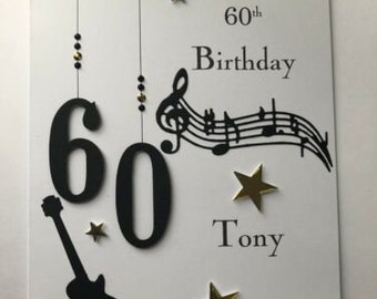 Könnte beinhalten: Eine weiße Karte mit schwarzen und goldenen Akzenten. Die Karte sagt "Happy 60th Birthday Tony" mit Noten und einer Gitarre.