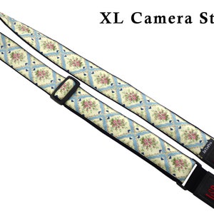 May include: A white and blue floral camera strap with black adjustable straps and the text "LSR" embroidered in red on the strap ends. The strap is labeled "XL Camera Strap".