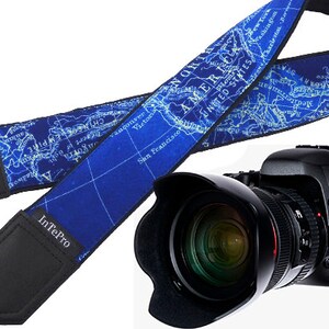 May include: A blue camera strap with a map design featuring the text "American Empire" and "United States". The strap is attached to a black camera with a large lens.