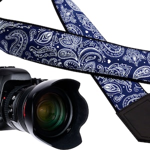 May include: A blue and white paisley camera strap with black leather accents. The strap is adjustable and has a padded shoulder section for comfort.