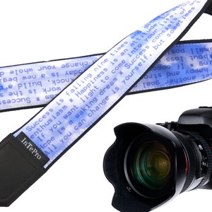 May include: A blue and white camera strap with the text "Success is falling nine times and getting up ten. Happiness is an attitude. If you want light to come into your dream, all you can change is yourself. But sometimes success consists of only one small step, or happy and strong stories. To set another goal." The strap is attached to a black camera with a large lens.