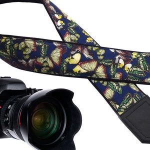 May include: A blue camera strap with a butterfly pattern. The strap is made of fabric and has a black leather pad.