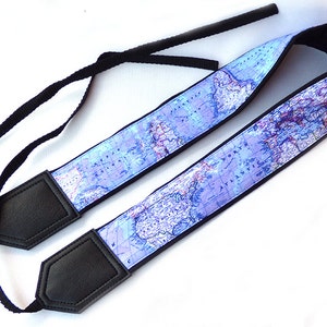 May include: A blue and purple camera strap with a world map design. The strap has black leather ends with a stitched design.