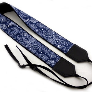 May include: A blue and white paisley camera strap with black adjustable straps and black leather ends.