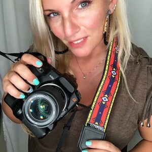 May include: A woman is holding a black camera with a red, yellow and blue patterned camera strap. The camera strap has the text "InTePro" on it. The camera has a lens with the text "0.52m/1.7ft MACRO" and "α200" on it.