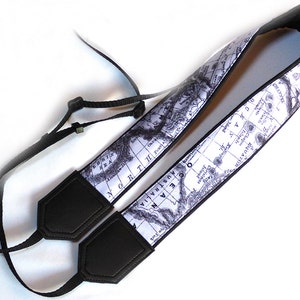 May include: A black camera strap with a white background featuring a vintage world map design. The strap has black leather padding on both ends.