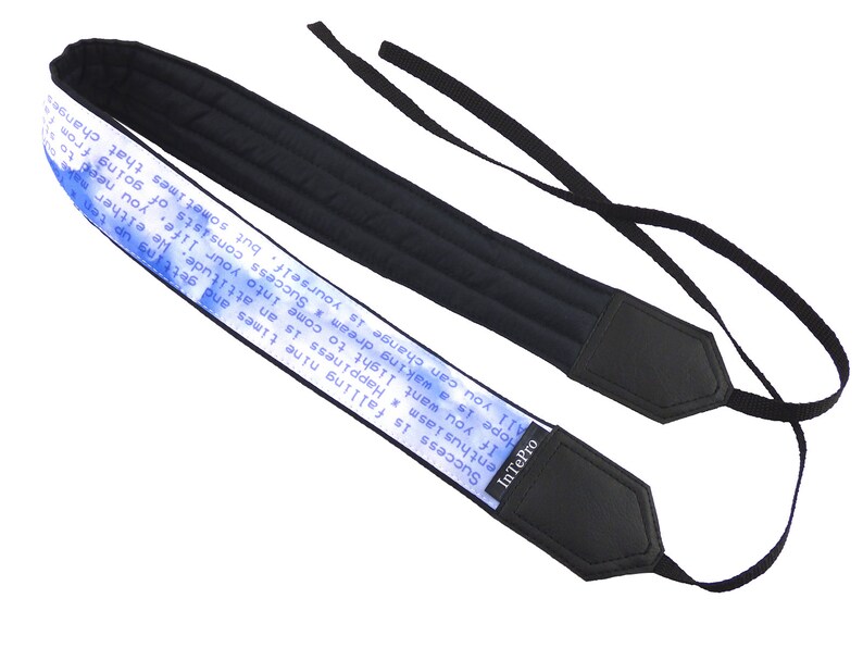 May include: Black camera strap with a blue and white printed quote that reads "Success is falling nine times and getting up ten. Happiness is an attitude. He either makes us stumble or he helps us to rise. If you want light to come into your life, you need to open your heart to the sun. All you can change is yourself, but sometimes that changes the whole world. Hope is a waking dream." The strap has a black leather end with the brand name "InTePro" printed on it.