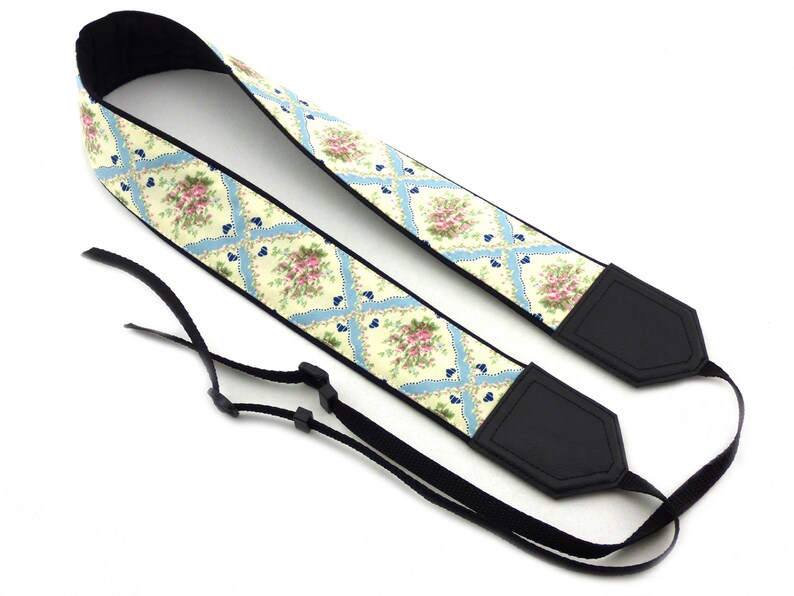 May include: A camera strap with a floral pattern in shades of pink, yellow, and blue. The strap is made of fabric and has black leather accents.