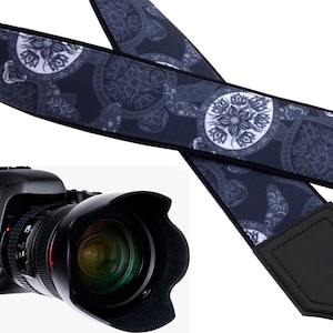 May include: A black camera strap with a white and gray floral pattern. The strap has a black leather pad and the text "InTePro" printed on the end.