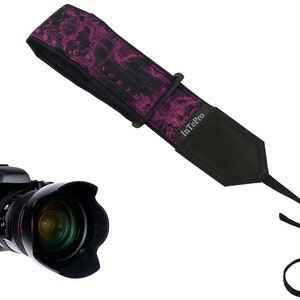 May include: A black camera with a lens and a pink and black camera strap with the text "InTePro" printed on it.