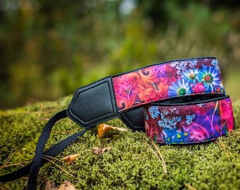 Puede incluir: Una correa de cámara colorida con un patrón floral en tonos de rosa, morado y azul. La correa tiene una almohadilla de cuero negro para mayor comodidad.