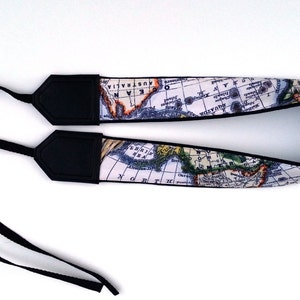 May include: A camera strap with a world map design. The strap is black with white and colored map details. The strap has two black adjustable straps.