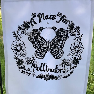 May include: A white garden flag with a black and white design featuring a butterfly, hummingbirds, and the text "A Place for Pollinators".