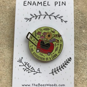 May include: Enamel pin on a white card. The pin features a red lawnmower filled with colorful flowers and the text "THE REVOLUTION OF A LAWN". The card has the text "ENAMEL PIN" and the website address www.TheBeesWeeds.com.