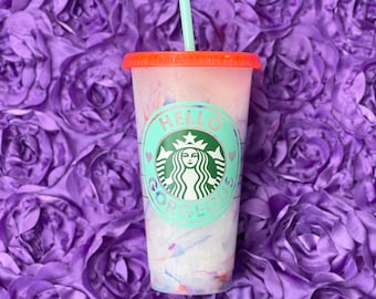 Może przedstawiać: Kubek wielokrotnego użytku w kolorze turkusowym i białym z czerwoną pokrywką i zielonym logo Starbucks. Na kubku widnieje napis "Hello Gorgeous".