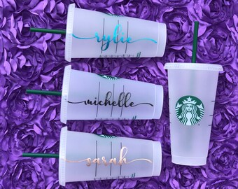 Könnte beinhalten: Drei durchsichtige Plastikbecher mit schwarzen Deckeln und Strohhalmen. Die Becher sind mit den Namen "Rylie", "Michelle" und "Sarah" in verschiedenen Farben verziert. Die Becher befinden sich auf einem violetten Hintergrund.