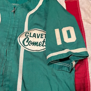 May include: Green baseball jersey with white accents and the number 10 on the sleeve. The jersey features the text "CLAVET Comet" in an oval patch on the chest. The jersey has a zipper and white trim.