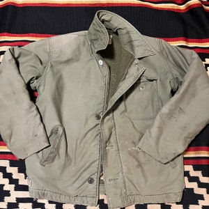 Puede incluir: Una chaqueta vintage verde forrada con cremallera y cierre de botones. La chaqueta tiene un bolsillo grande en el lado izquierdo y un bolsillo más pequeño en el lado derecho.