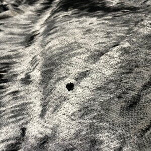 K&ouml;nnte beinhalten: Nahaufnahme eines schwarz-wei&szlig;en Stoffes mit einem kleinen schwarzen Loch in der Mitte.