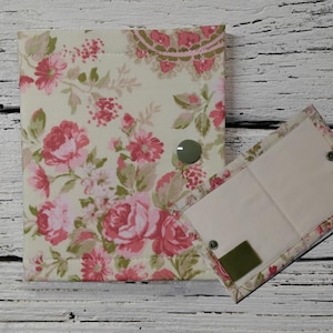May include: A floral fabric journal and matching case. The journal and case feature a cream background with pink roses and green leaves. The journal has a green button closure. The case is open, revealing a blank interior.