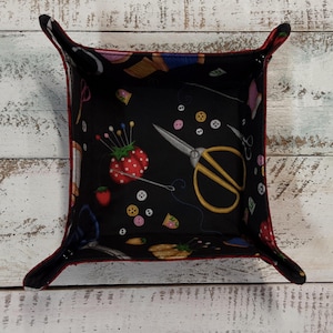 May include: A red and black fabric storage tray with a sewing themed print. The print features scissors, buttons, needles, thread, and strawberries.