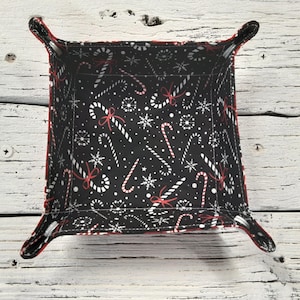 May include: A black fabric storage tray with red and white candy cane and snowflake pattern. The tray has two fabric handles.