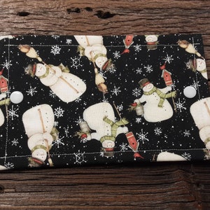 May include: Black fabric with a white snowman pattern. The fabric has white buttons on the sides. The fabric is a Christmas themed design.