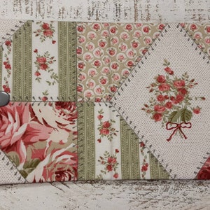 May include: A patchwork fabric pouch with a floral design in shades of pink, green, and white. The pouch has two silver buttons and is sewn with a decorative stitch.