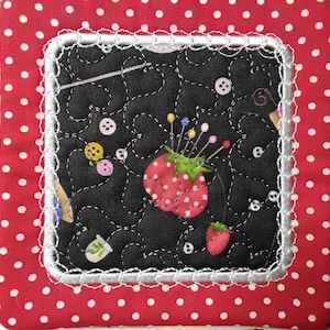 May include: A square, quilted coaster with a red polka dot border and a black center. The center features a strawberry pincushion, sewing notions, and buttons. The coaster is trimmed with white lace.
