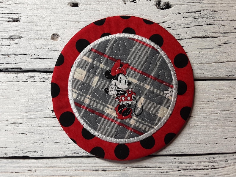 May include: Red and black polka dot fabric coaster with a white and gray plaid fabric center featuring a cartoon image of Minnie Mouse.