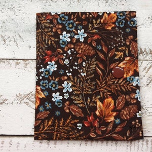 May include: A brown fabric pouch with a floral pattern featuring blue flowers, brown leaves, and orange accents. The pouch has a brown button closure.