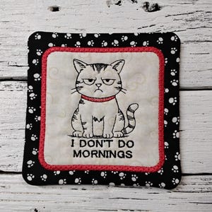 May include: Square coaster with a grumpy cat illustration. The cat is gray and white with a red collar, and the text reads "I DON'T DO MORNINGS." The coaster has a black border with white paw prints and a red inner border.