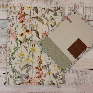 May include: A floral-patterned notebook and matching square notepad. The notebook and notepad feature a cream background with colorful wildflowers in red, yellow, and pink. The notepad has a light green polka dot accent.