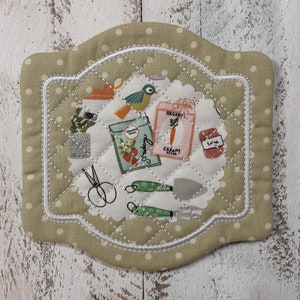 May include: A green quilted pot holder with white polka dots and a white stitched border. The center features a white scalloped circle with a gardening themed print, including a bird, seed packets, and gardening tools.