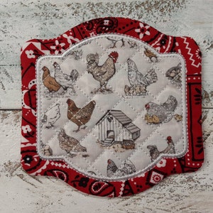 May include: A red and white quilted fabric coaster with a white embroidered border. The coaster features a pattern of chickens and a small white coop.