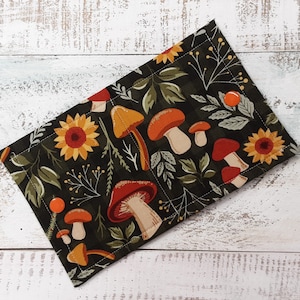 May include: A green fabric pouch with a mushroom and sunflower pattern. The pouch has orange buttons.