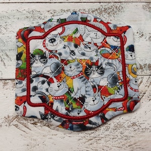 May include: A red and white quilted fabric coaster with a red stitched border. The coaster features a pattern of cats in various poses.