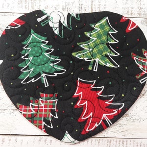 May include: A black heart-shaped quilted hot pad with a Christmas tree pattern. The trees are green, red, and plaid with white outlines. The background is black with white polka dots.