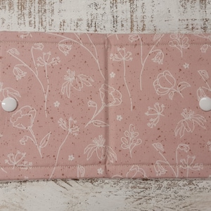 May include: A pink fabric pad with a white floral pattern and white snap buttons on each side. The pad is made of a soft, quilted fabric and is perfect for protecting surfaces from scratches and spills.